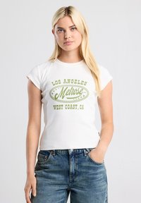White ribbed short-sleeve T-shirt featuring green text: "LOS ANGELES Melrose WEST COAST, CA," paired with faded blue jeans.