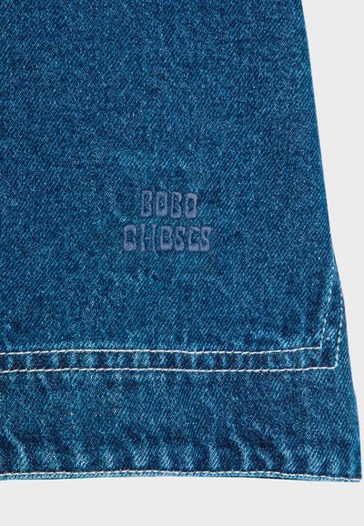 Tessuto di denim blu con una superficie texturizzata, caratterizzato da un orlo cucito visibile e da una scritta stampata che recita "BOBO CHOSES" in blu scuro.