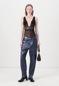 Body negro de encaje con escote en V profundo, combinado con jeans de pierna ancha brillantes en azul y un pequeño bolso negro con correa para el hombro.