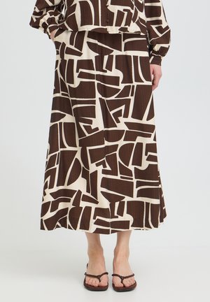 Mujer con falda midi de patrón abstracto en marrón y beige, con top a juego y sandalias marrón oscuro con tiras trenzadas.