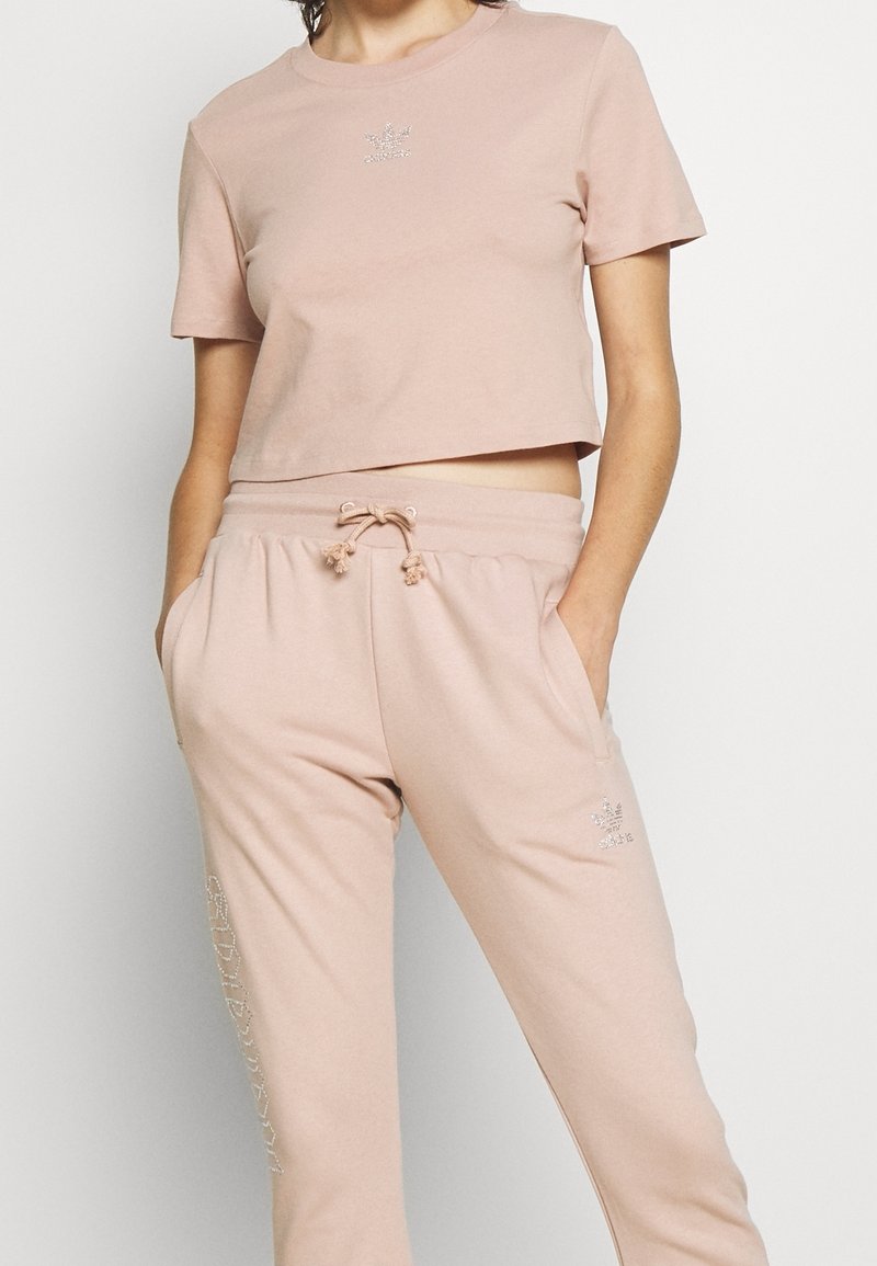 Ljusrosa kortärmad t-shirt med korta ärmar och en liten silverlogotyp på bröstet, tillsammans med matchande sweatpants med dragstring och fickor.