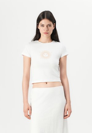 White cropped t-shirt with short sleeves and a sun graphic in light orange at the center, paired with a white skirt. Smooth texture.