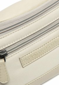 Lichtbeige pouch gemaakt van gestructureerde stof met twee ritsen en een leren label, voorzien van een gladde ritsaftrekker en gestikte accenten.