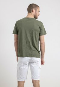 T-shirt en coton vert olive à manches courtes, présenté de dos. Porté avec un short cargo blanc doté de poches latérales.
