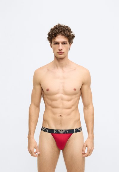 Cueca tanga vermelha com cintura elástica preta com um logótipo. Textura suave, design ajustado e forma contornada.