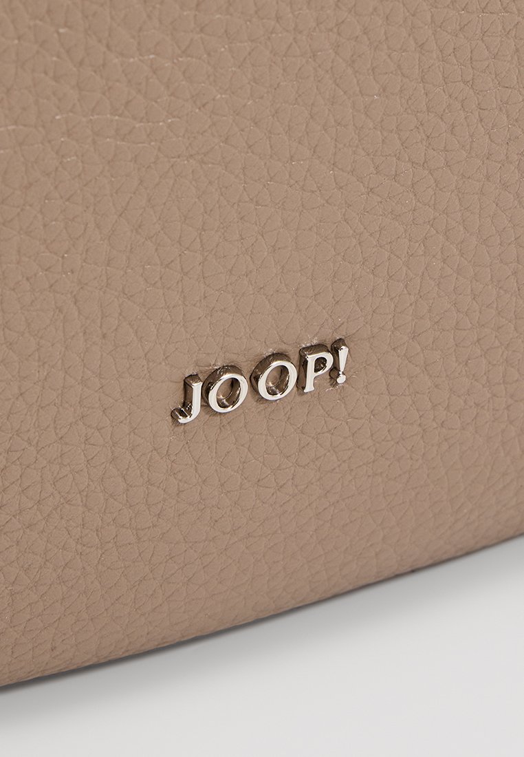 Beżowa skórzana torba o teksturowanej powierzchni. Zawiera wytłoczone na srebrno logo "JOOP!". Skupia się na materiałach, kolorze i detalu logo.