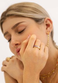 Anillo multicolor con piedras rectangulares en un engaste de oro, llevado en la mano. La piel suave y la delicada joyería acentúan el diseño.