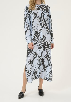 Femme portant une robe midi à manches longues boutonnée avec un motif abstrait noir et bleu clair et des chaussures slingback noires à bout pointu.