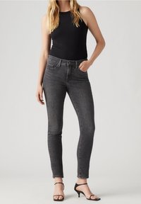 Svart ribbad linne i kombination med mörkgrå slim-fit jeans. Jeansen har framfickor och ett subtilt blekt mönster, vilket kompletteras av svarta klackar.