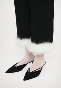 Svarte bukser med hvit, fluffy kant, kombinert med svarte spissede hæler med tynne stropper. Rene linjer og kontrasterende teksturer.