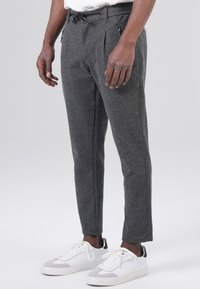 Gray, tailored pants with a textured fabric, pleated front, drawstring waist, and zippered side pockets, paired with white sneakers.