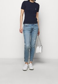 Navy knitted short-sleeve sweater, light blue ripped jeans, white sneakers, and a small white handbag with a chain strap.