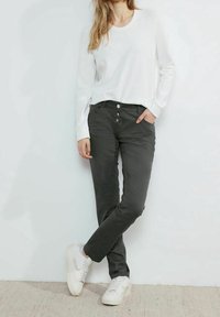 Haut blanc à manches longues en tissu texturé, associé à un pantalon gris slim avec braguette boutonnée et poches avant. Baskets blanches.