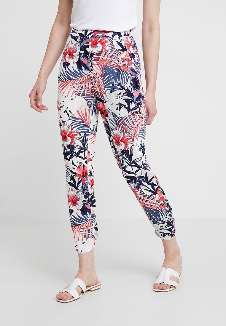 Pantalons à motif tropical avec un fond blanc et des fleurs rouges et bleu marine, taille élastique et chevilles ajustées.