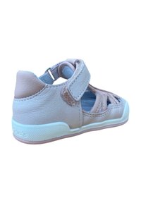 Sandalia de cuero rosa claro con tira de velcro, diseño abierto, acentos texturizados y suela de goma blanca con un patrón sutil.