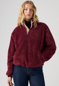 Burgundski flis pulover z zadrgo na ovratniku, z teksturirano tkanino, elastičnim robom in kontrastno bež notranjo plastjo.