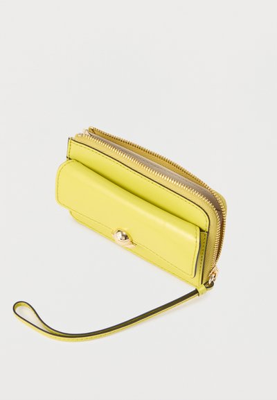 Petit porte-monnaie bracelet en cuir jaune avec une poche à rabat à l'avant et deux compartiments zippés dorés sur un fond blanc.