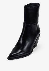 Bota de tobillo de cuero negro con punta afilada, silueta angular y tacón grueso. Textura suave y detalle de costura mínima.