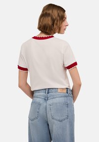Vit kortärmad t-shirt med röd vågig halsringning och ärmslut, tillsammans med ljusblå högmidjade jeans med bakfickor.