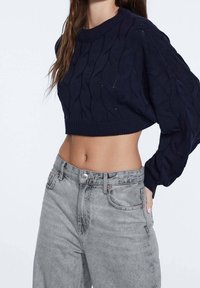 Pull court en maille torsadée bleu marine à manches longues, associé à un jean en denim gris clair taille haute avec fermeture à boutons et poches avant.