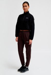 Sort cropped sweatshirt med høj krave og logo, kombineret med brune joggers med elastisk talje og sidelommer. Sorte sneakers.
