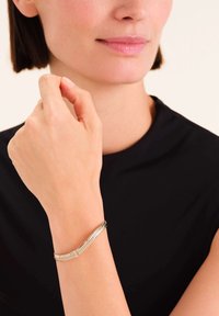 Bracciale in tonalità argento con motivo a spina di pesce, texture liscia e un sottile dettaglio in pietra preziosa, indossato in un primo piano di una mano.