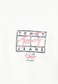 Tommy Jeans logo med sorte omrissede bokse, rød kursiv "Tommy" og teksten "NYC 1985 NYC Registreret Varemærke" på hvid baggrund.