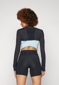 Athletic outfit featuring a black long-sleeve top with mesh accents and a light blue crop underneath, paired with high-waisted black shorts.