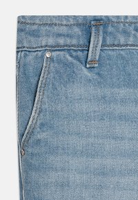 Ljust blå denimtyg med en diagonal vävstruktur, som har en framficka med en metallnail och kontrasterande orange sömnadsdetaljer.