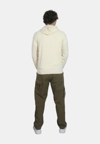 Felpa crema con una vestibilità morbida, orlo a coste e tasca a marsupio, abbinata a pantaloni cargo oliva con più tasche e gamba affusolata.