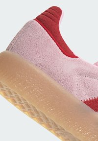 Roze suede sneaker met een rode accenten, een textuur oppervlakte en een doorschijnende rubberen zool met een geometrisch patroon.