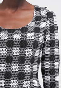 Długi rękaw top w teksturowanej czarno-białej tkaninie z geometrycznym wzorem heksagonów i kółek oraz okrągłym dekoltem.