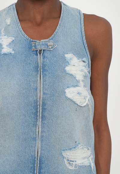 Hele sinise denimi ilma varrukatega vest, millel on mitmed kulunud plekid ja hargnenud servad. Omab eeslibisevat tõmblukk ja metallist nupulukku. Sile tekstuur.