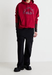 Rode hoodie met de tekst "GAP Athletic 1969", gecombineerd met zwarte cargo pants met zijzakken en zwarte platform schoenen.