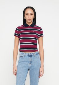 Polo tričko s krátkym rukávom s námorníckymi modrými a bordovými pruhmi, s golierom a zapínaním na tri gombíky, kombinované s vysokým pásom svetlých džín.