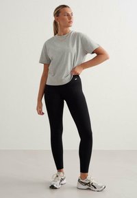 Graues Baumwoll-T-Shirt mit kurzen Ärmeln, kombiniert mit schwarzen gerippten Leggings. Silberne Sportschuhe und minimaler Goldschmuck runden den Look ab.