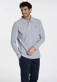 Polo-shirt à manches longues gris clair avec col et un détail de logo subtil. Associé à un pantalon marine, présentant une texture douce et une coupe classique.