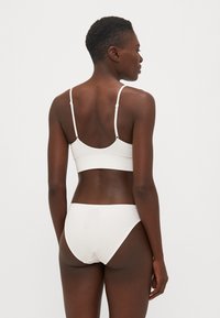 Fehér bordázott bralette vékony pántokkal, zökkenőmentes kialakítással, és egy hozzá illő bordázott bikini alsóval. Sima textúra, egyszerű esztétika.