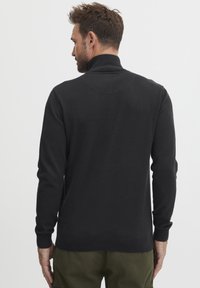 Pullover negro de manga larga con cuello alto y puños acanalados. Presenta una textura de punto suave y un discreto detalle de costura en la parte posterior.