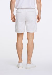 Pantalones cortos de algodón blancos con una superficie texturizada, que presentan dos bolsillos traseros y un ajuste casual, combinados con zapatillas blancas.