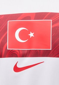 Κόκκινη και λευκή τουρκική σημαία πάνω από το κόκκινο λογότυπο Nike swoosh σε λευκό ύφασμα με κόκκινη ριγωτή διακόσμηση.