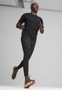 Czarny sportowy T-shirt i legginsy, z subtelnym logo, w połączeniu z zielonymi i pomarańczowymi butami do biegania. Gładki, dopasowany krój do swobodnego ruchu.