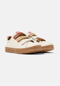 Baskets en cuir crème avec des bandes Velcro marron et beige, semelle en caoutchouc avec des éclats, et marquage rouge sur la languette. Design décontracté.