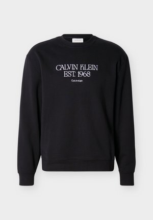 Svart crewneck-genser med hvit tekst "CALVIN KLEIN EST. 1968" og mindre "Calvin Klein" brodert på brystet.