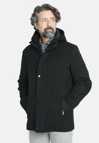 Abrigo negro de mezcla de lana con capucha, que incluye cierre frontal de cremallera, botones de presión, bolsillos laterales y textura suave. Detalles notables de costura.