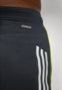 Shorts de sport noirs en matériau qui évacue l'humidité, avec des rayures blanches et un accent vert fluo sur le côté, présentant le logo "AEROREADY".
