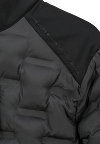 Schwarze gepolsterte Jacke am Schulterbereich mit strukturiertem Stoff und dezentem Text "Authentic Urban Explorer // Devaix."