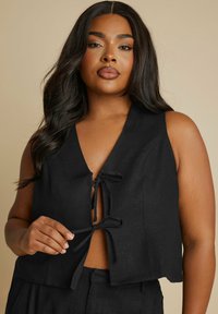 Svart kort topp i texturerad tyg med V-ringning och detaljer som knyts fram. Ärmlös design med avslappnad passform.