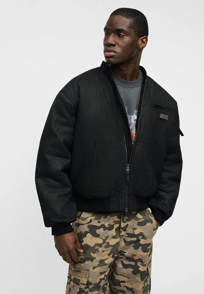 Μαύρο μπουφάν bomber με φερμουάρ μπροστά, με τσέπη με φερμουάρ στο στήθος, σε συνδυασμό με καμουφλάζ παντελόνι cargo. Ομαλό ύφασμα, άνετη εφαρμογή.