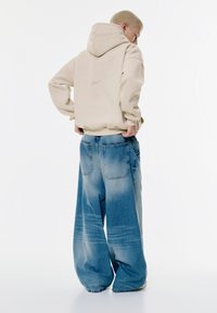 Beige mikina s kapucňou s voľným strihom, spárovaná s oversized svetlomodrými džínsami s vyblednutým umývaním a štyrmi vreckami.